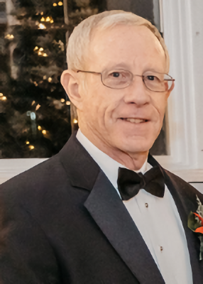 Photo of Andy Loerch, a man with gray hair and glasses. He is wearing a tuxedo and smiling at the camera.